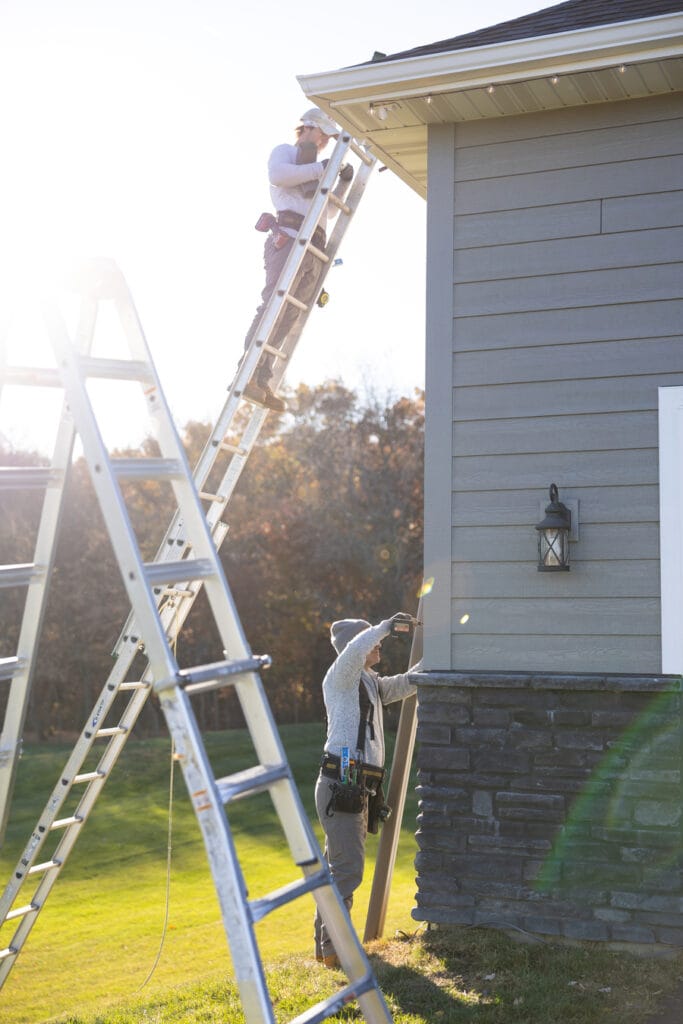 Technician installing a vertical downspout and securing gutter hardware on a residential home in Delano.