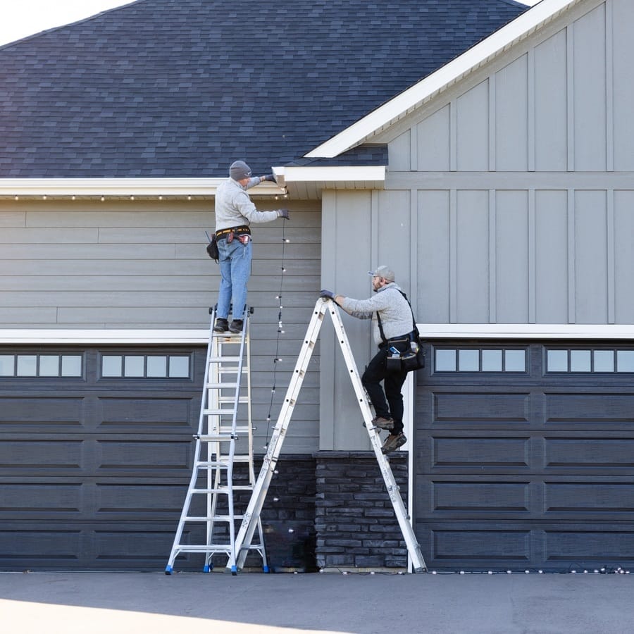 Two team members on ladders performing exterior roofline services on a large residential garage.
