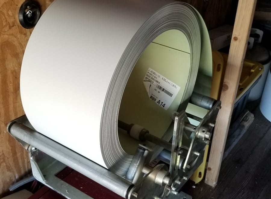 A large roll of white aluminum coil loaded into a seamless gutter machine inside a service trailer.