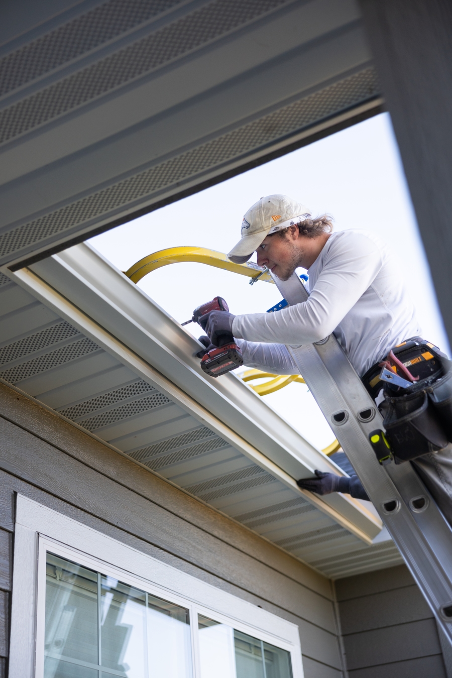 Vertical shot of two technicians on ladders using hand tools to custom-fit a seamless gutter corner.
